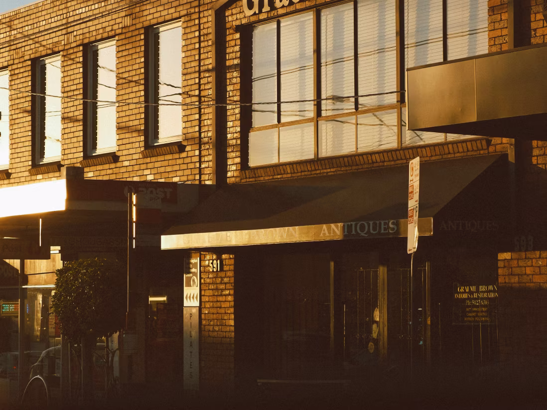 Brick building with multiple windows reflecting sunlight and an awning labeled 'ANTIQUES' over a storefront.