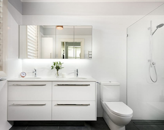 Modern bathroom with white double sink vanity, large mirror, white toilet, and glass-enclosed shower.
