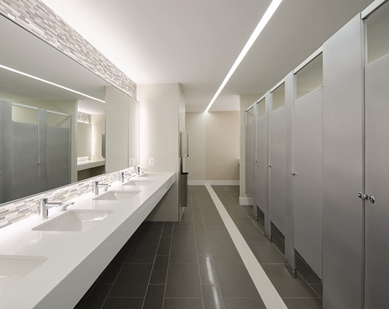 Modern commercial bathroom with multiple sinks and large mirror on left and a row of closed gray stalls on right.