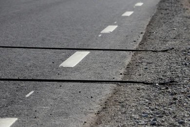 Close-up of a paved road with white dashed lane markings and a gravel shoulder.