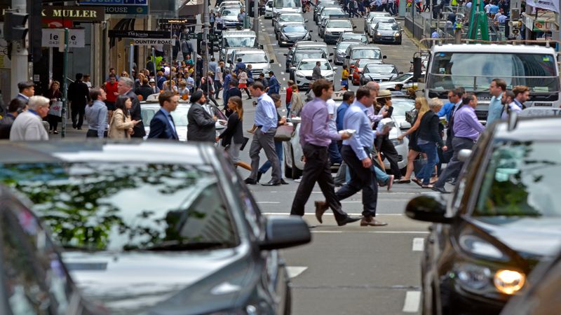 Crowded city street with many people crossing and vehicles waiting in traffic.