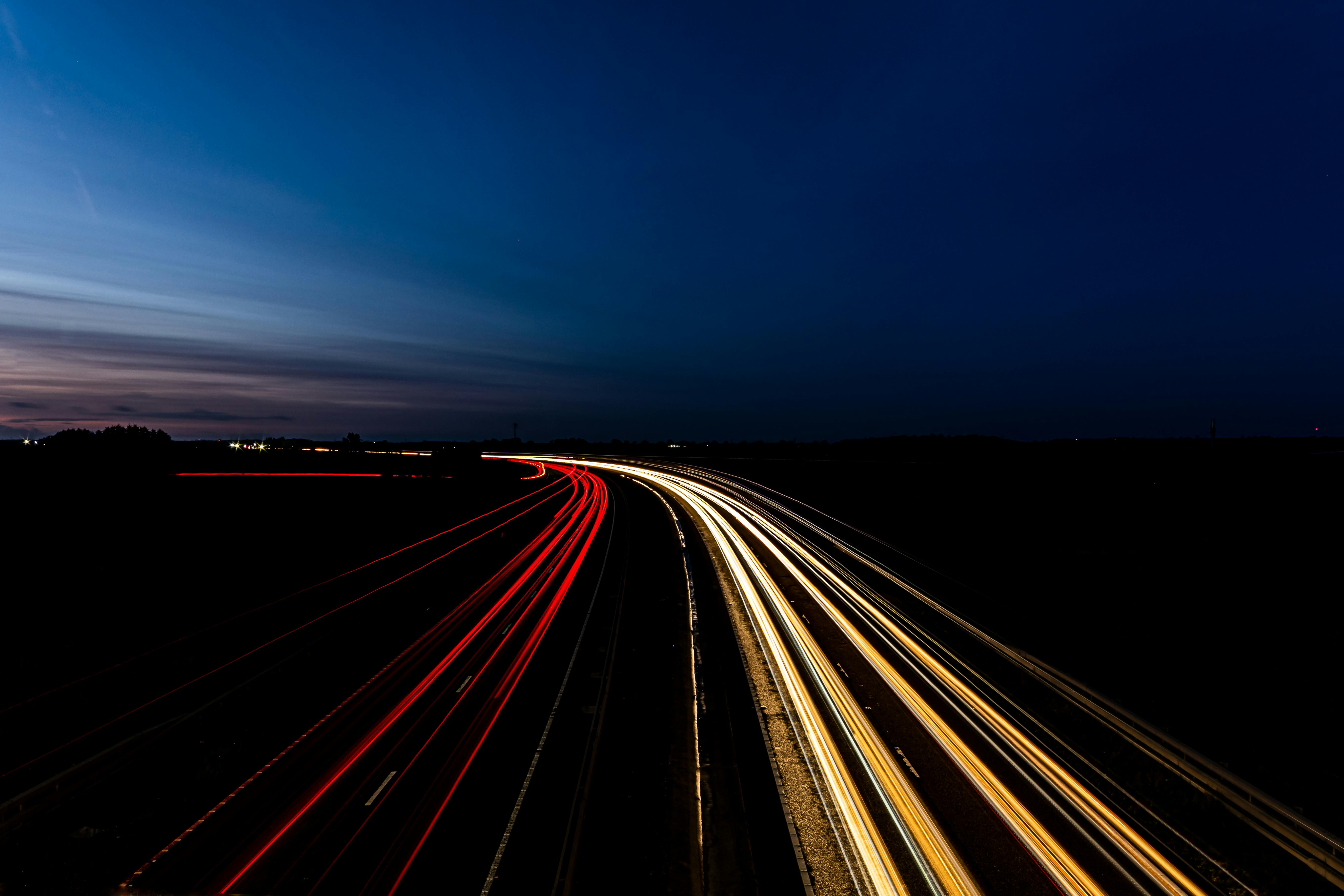 Light trails of red and white headlights on a highway at dusk under a darkening blue sky.