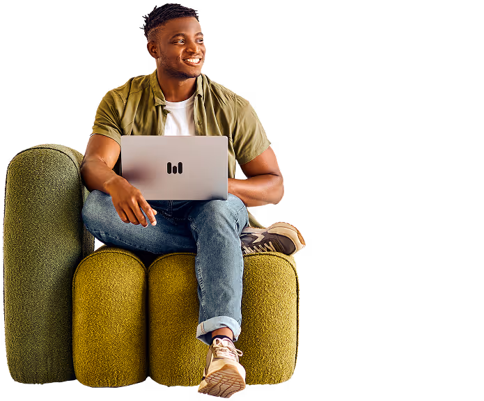 Smiling man sitting cross-legged on green chair working on a laptop with a black logo.