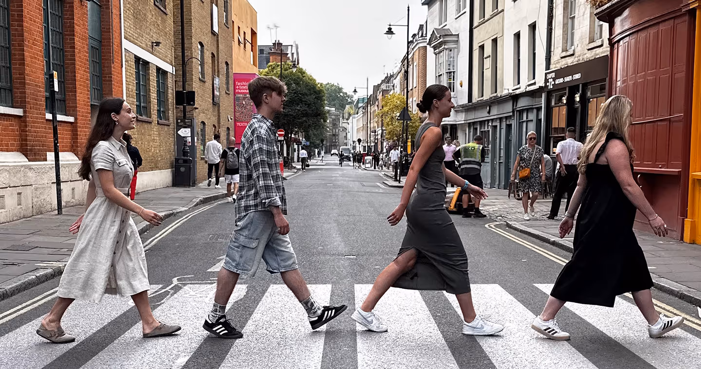 Four people walking across a city zebra crosswalk between urban buildings.