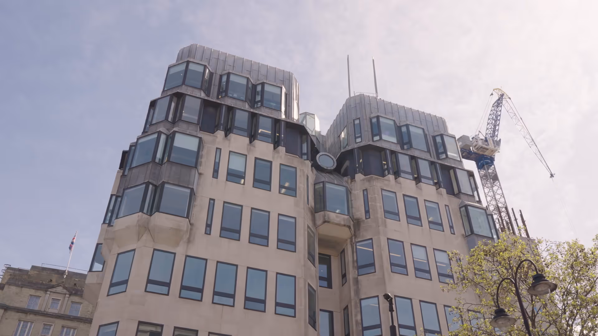 Modern multi-story building with large windows, a curved metal roof, and a construction crane in the background.