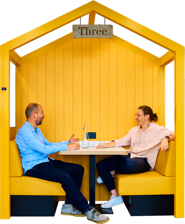 Two men seated in a yellow booth shaped like a house talking over a table with drinks.