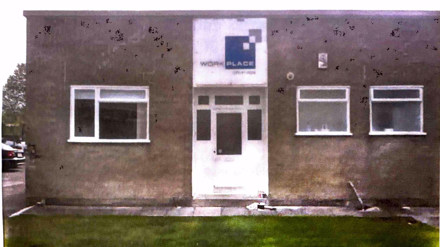 Plain brown building with three windows and a white door with a Workplace Creations sign above it.