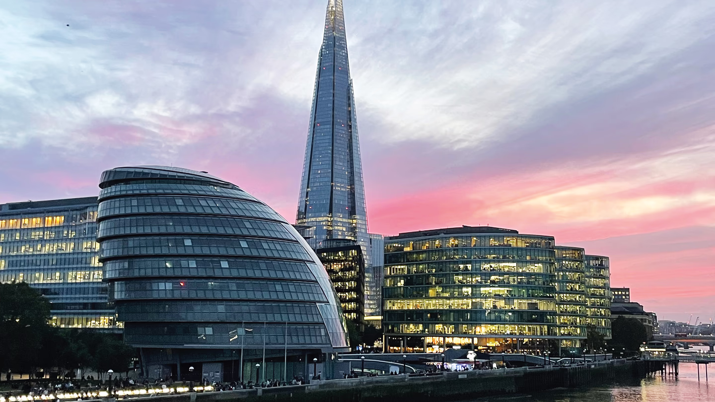 The Shard and modern buildings glowing at sunset along the River Thames in London.