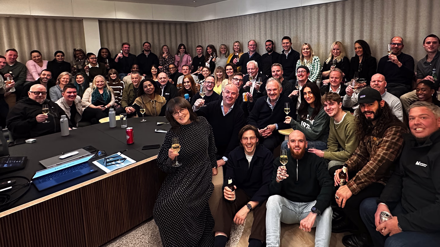 Group of diverse adults at a celebratory gathering holding drinks and smiling in an indoor room.
