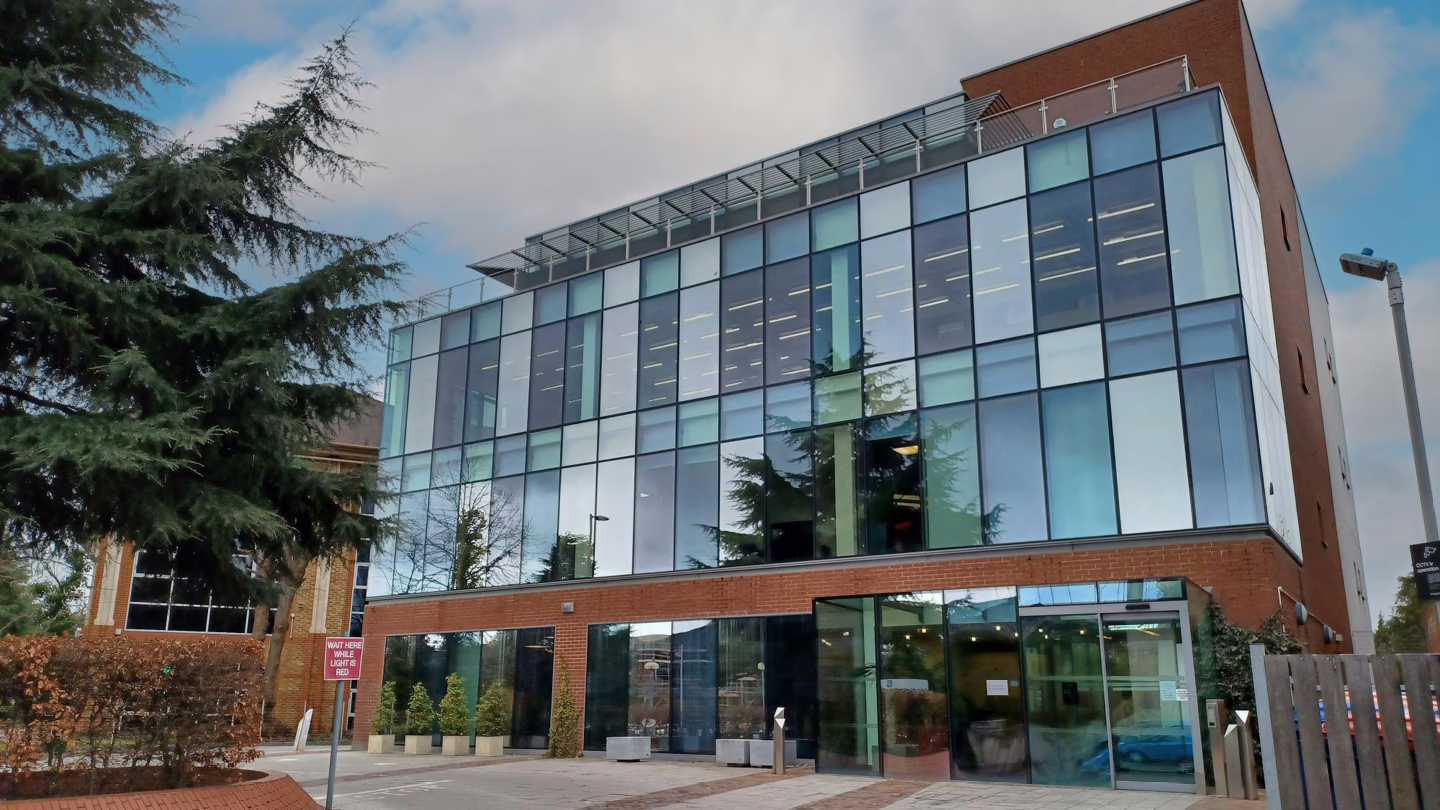 Modern three-story building with large glass windows and brick accents under a blue sky.