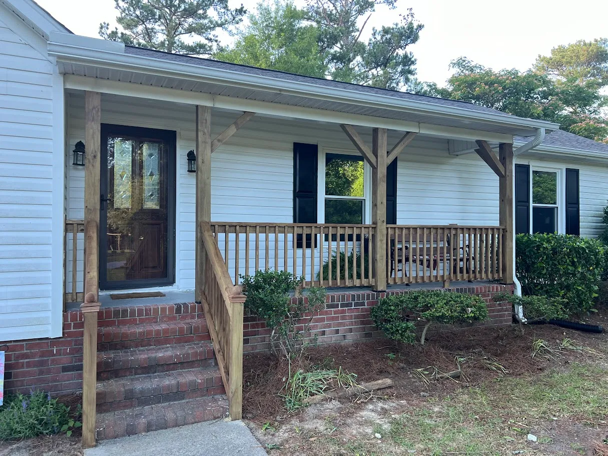 White house front porch with natural wood railing, brick steps, and black shutters on windows.