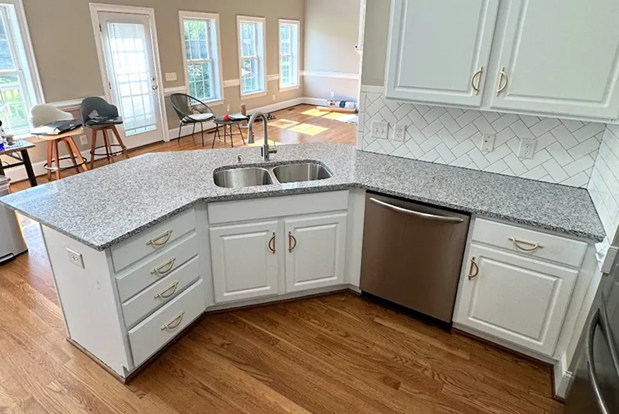 Modern kitchen corner with light gray speckled granite countertops, white cabinets, stainless steel sink, and dishwasher on wood flooring.