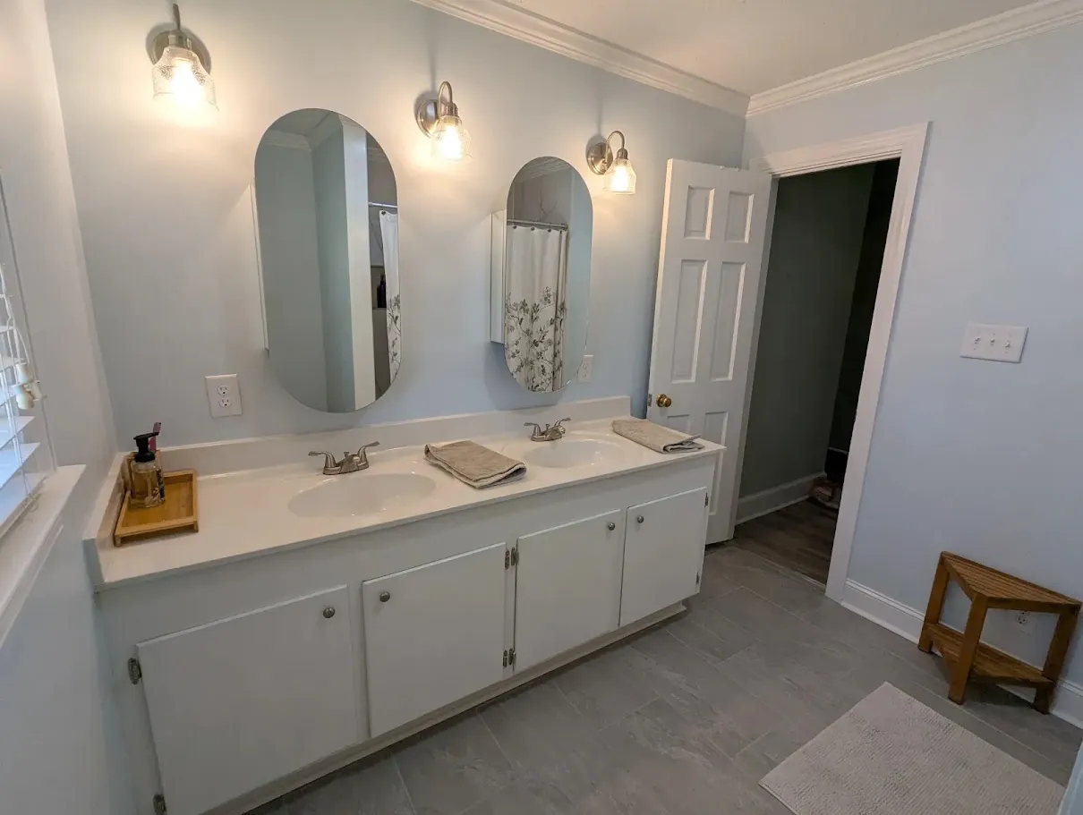 A Greenville, NC bathroom that has been completely remodeled by Unleashed Renovations with a new sink, new countertops, new mirrors, and new flooring 