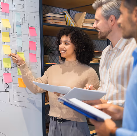 Three colleagues collaborating by a whiteboard with sticky notes and diagrams in an office setting.