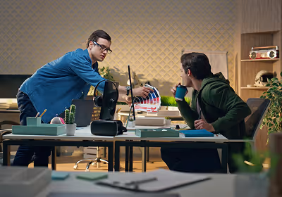 Two men in an office reviewing color swatches, one standing and pointing while the other sits holding a cup.