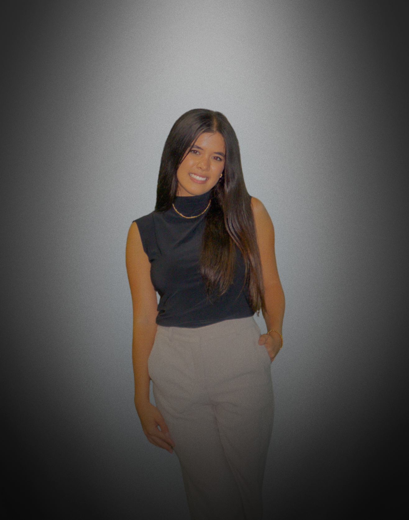 Smiling woman with long dark hair, wearing a sleeveless black top and light-colored pants, standing against a dark gradient background.