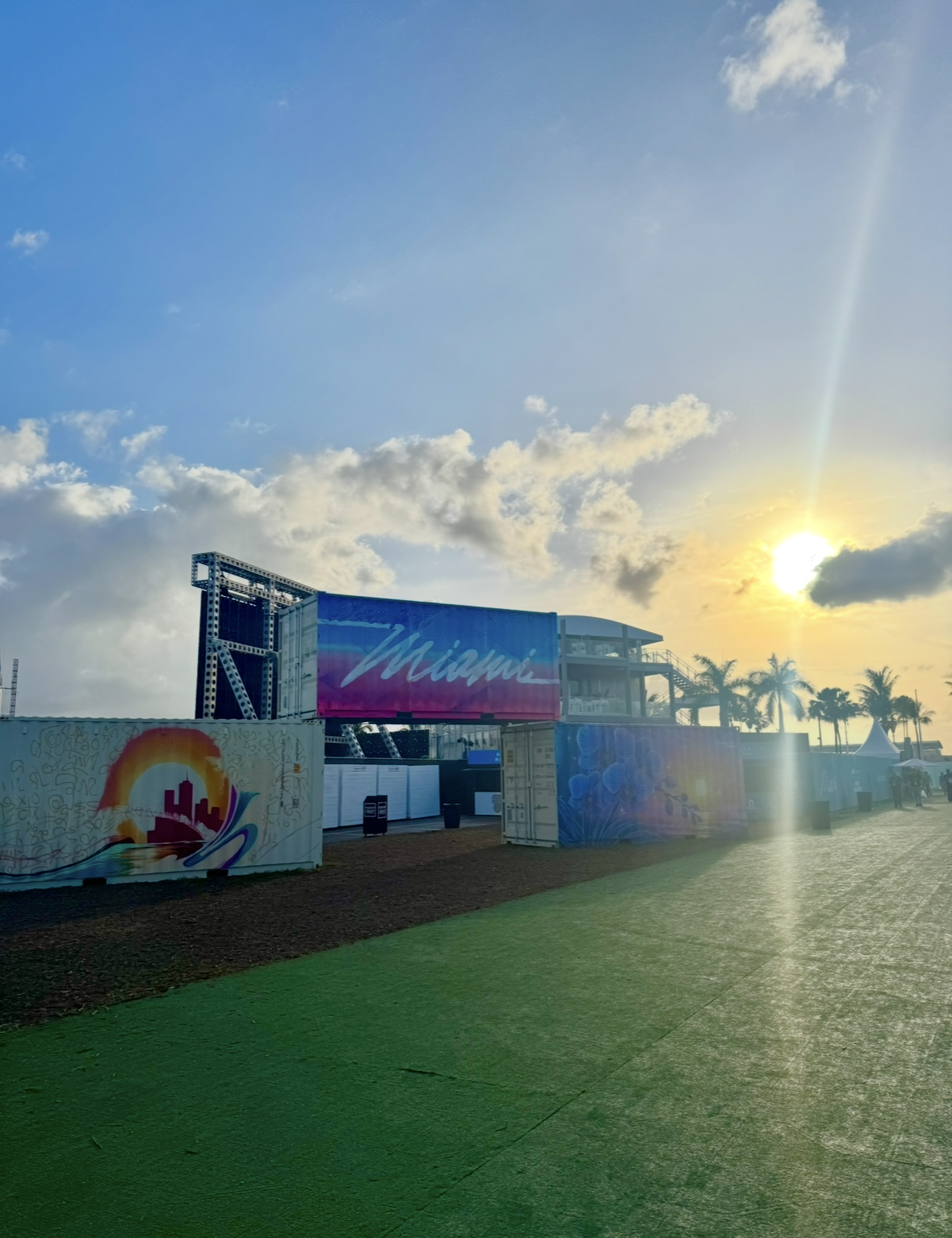 Sunset over an outdoor event area with decorated shipping containers and palm trees in Miami.