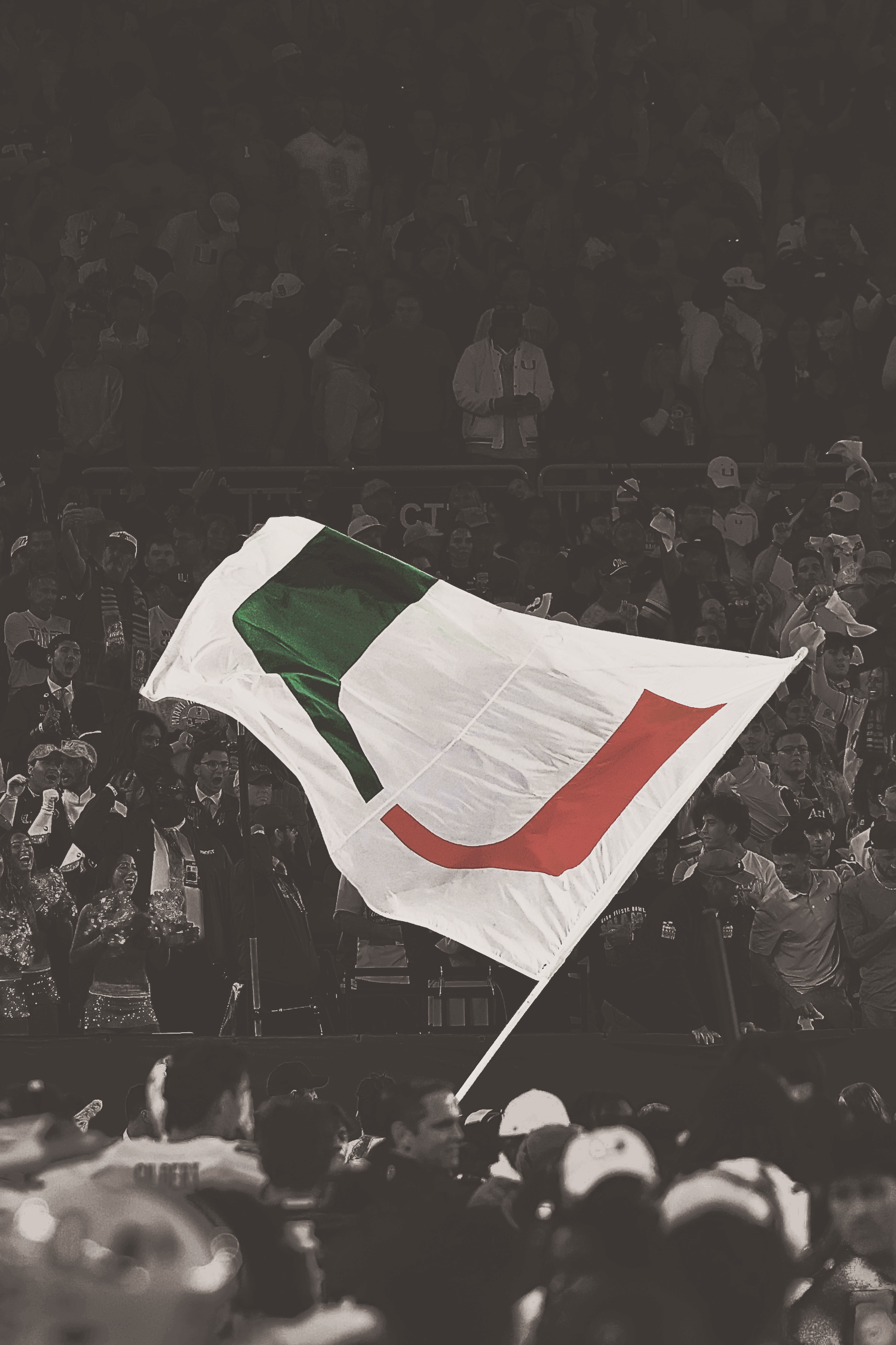 Large white flag with a green and orange stylized 'U' being waved by fans in a crowded stadium.