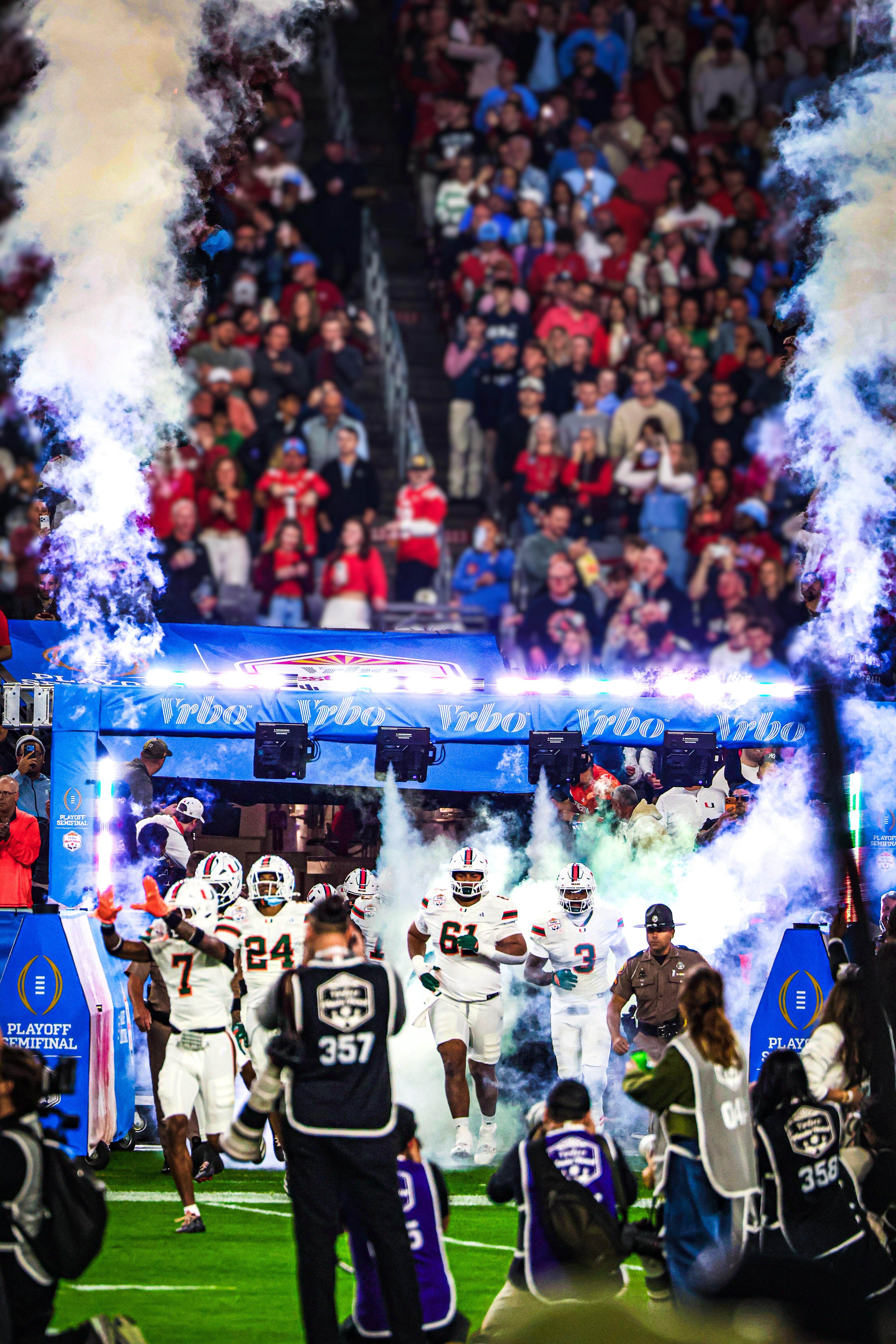 College football players in white uniforms running out of a tunnel with smoke and pyrotechnics during a playoff semifinal entrance.
