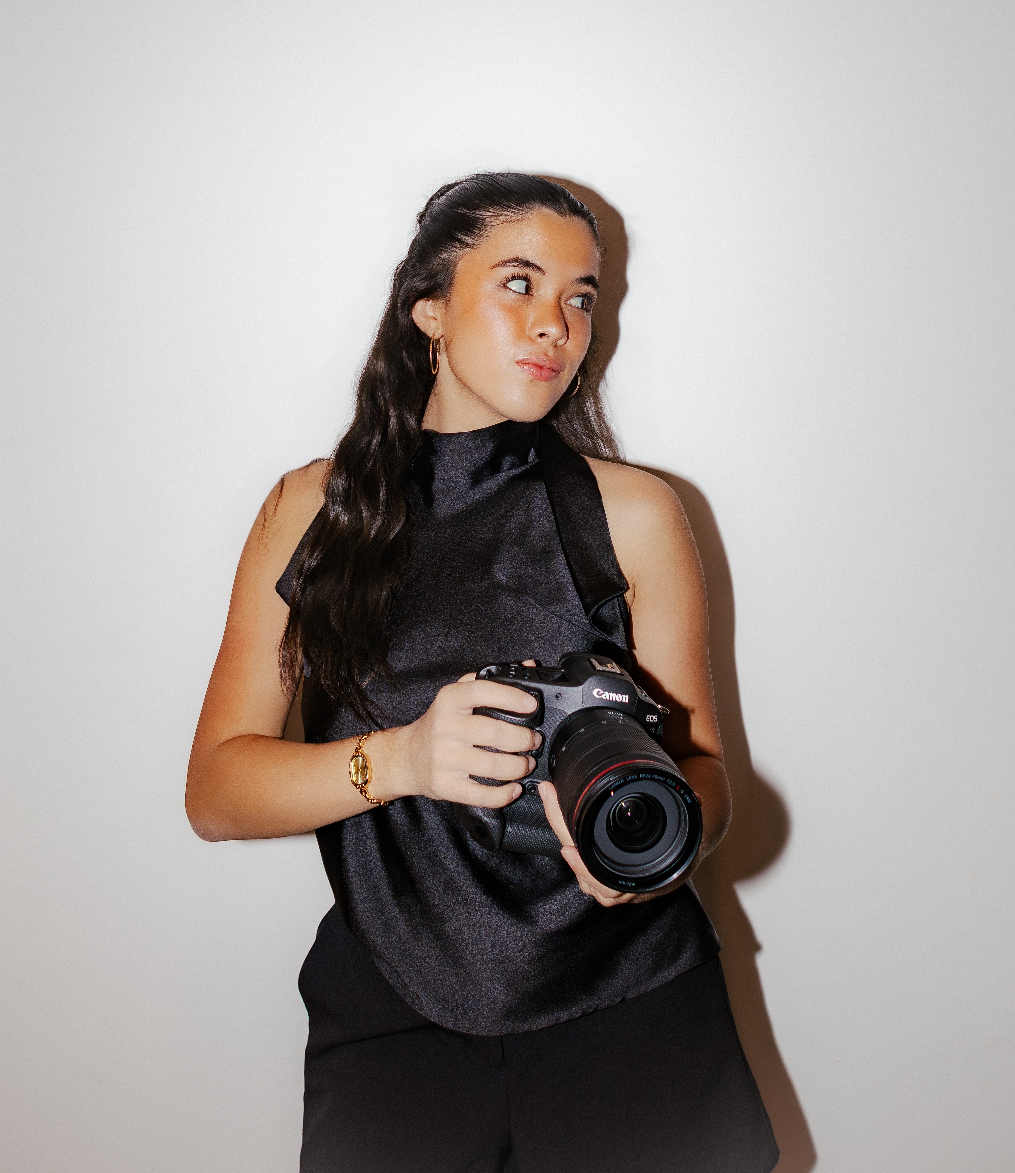 Young woman in black sleeveless top holding a Canon camera, looking to her right.