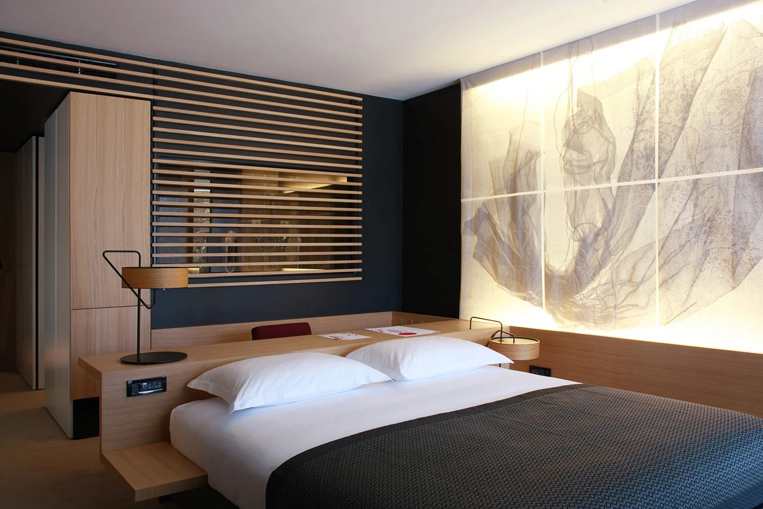 Lone bedroom with backlit wall panel and blinds