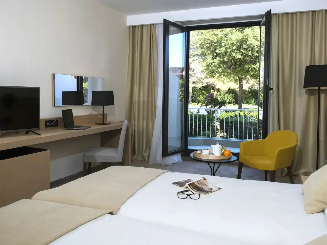 Hotel Liburna twin room with yellow armchair and balcony door to the garden