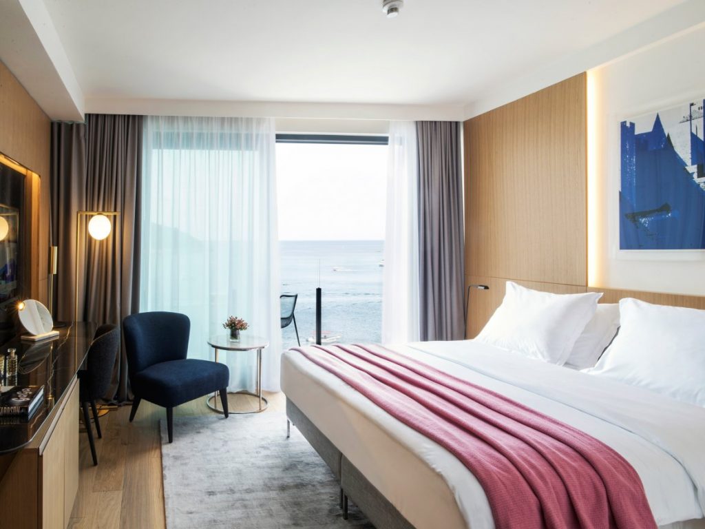Hotel Excelsior double bedroom with pink throw, blue armchair and balcony