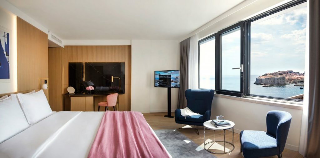 Hotel Excelsior bedroom with blue armchair, TV and large windows