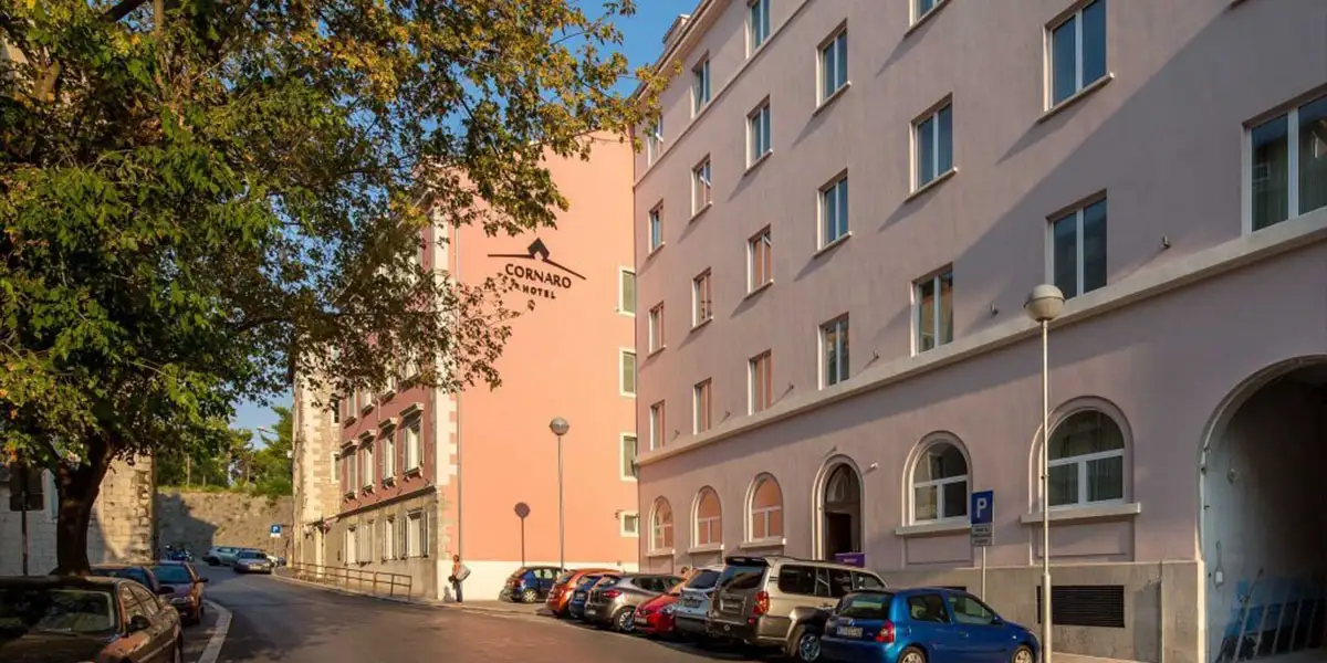 Hotel Cornaro pink and white facade on a tree-lined street