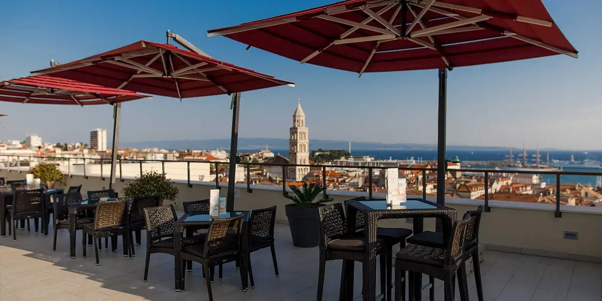 Hotel Cornaro rooftop terrace with red parasols and old town bell tower view