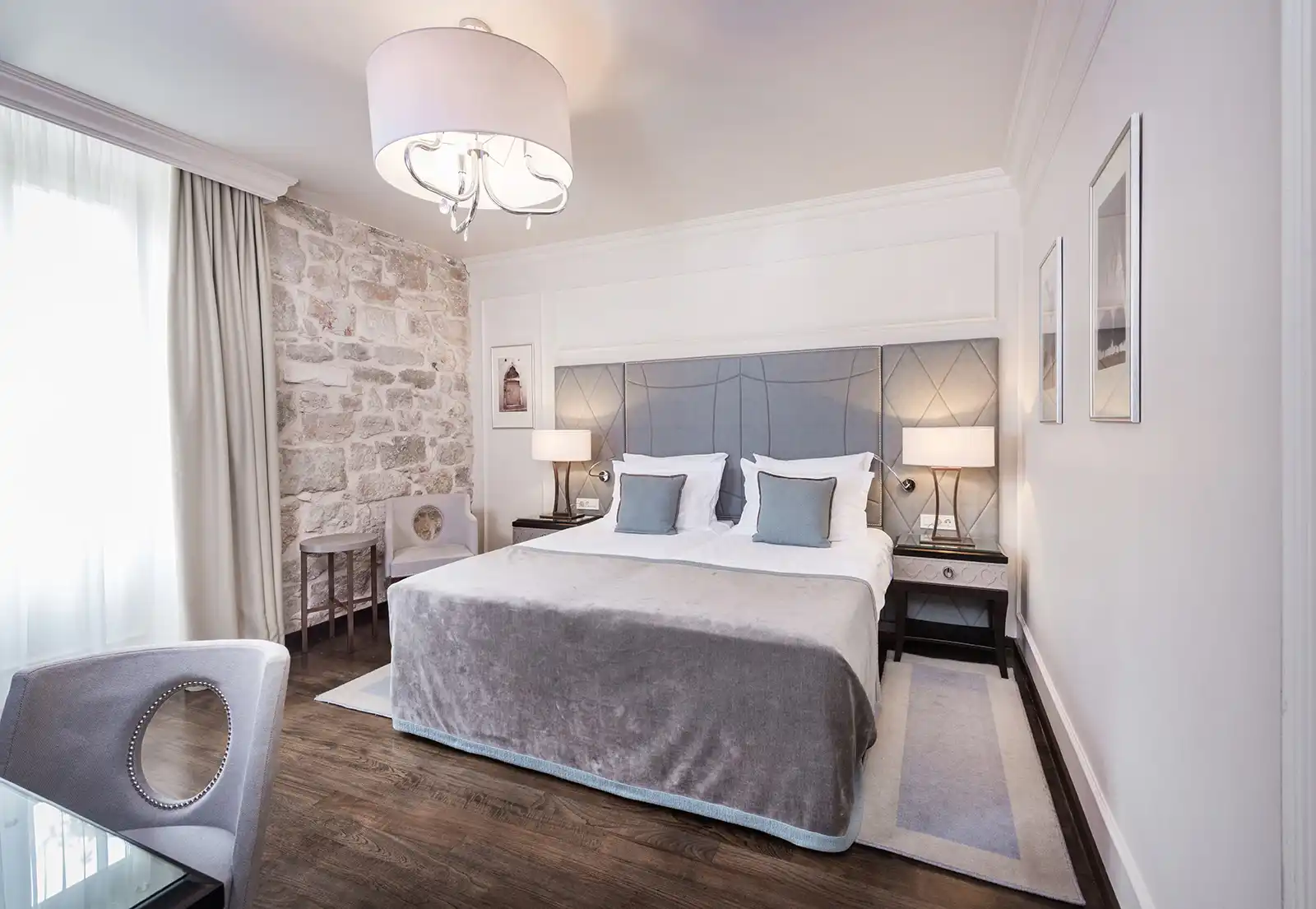 Boutique Hotel Bastion bedroom with grey padded headboard, chandelier and stone accent wall