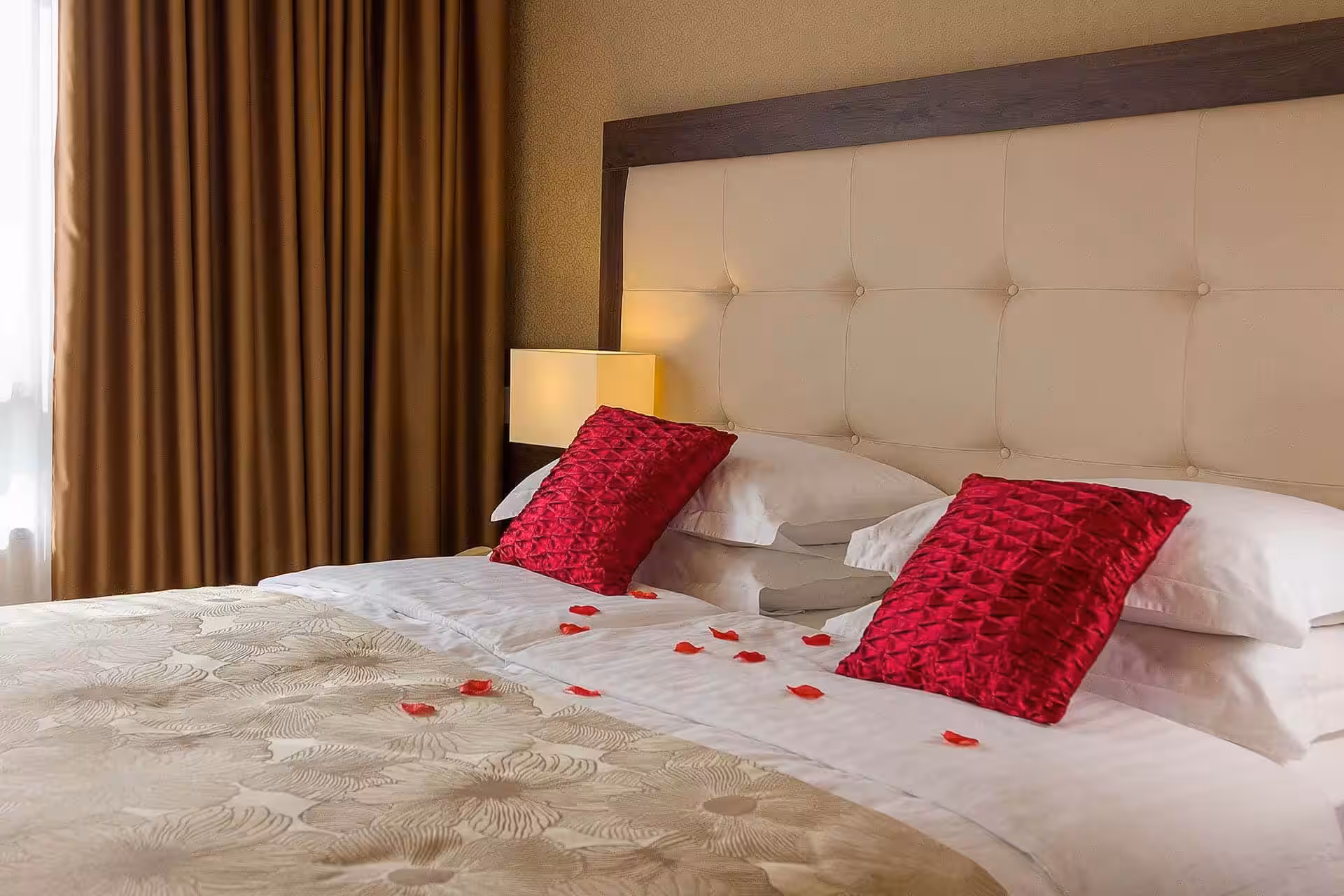 Degenija Hotel bed with red cushions and scattered rose petals
