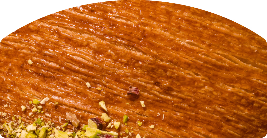 Close-up of a glossy brown textured pastry topped with crushed pistachios and bits of dried fruit.