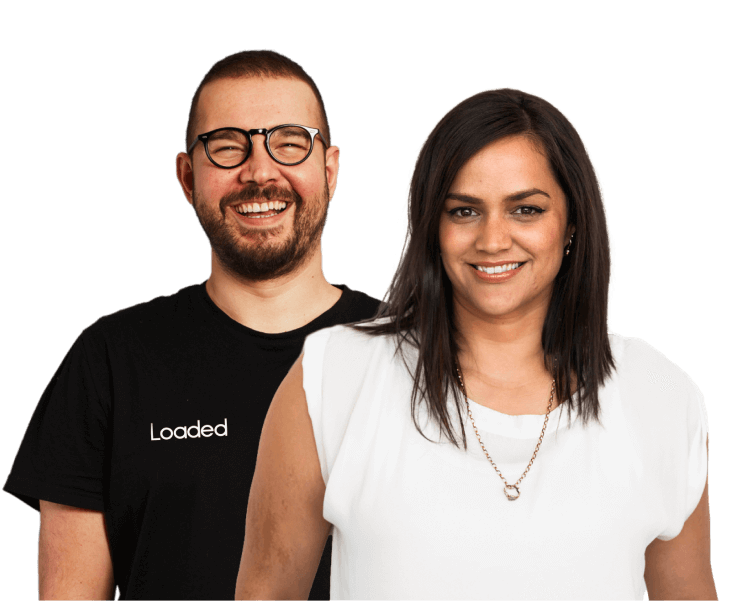 Smiling man wearing glasses and a black Loaded t-shirt standing behind a smiling woman with dark hair in a white top and necklace.