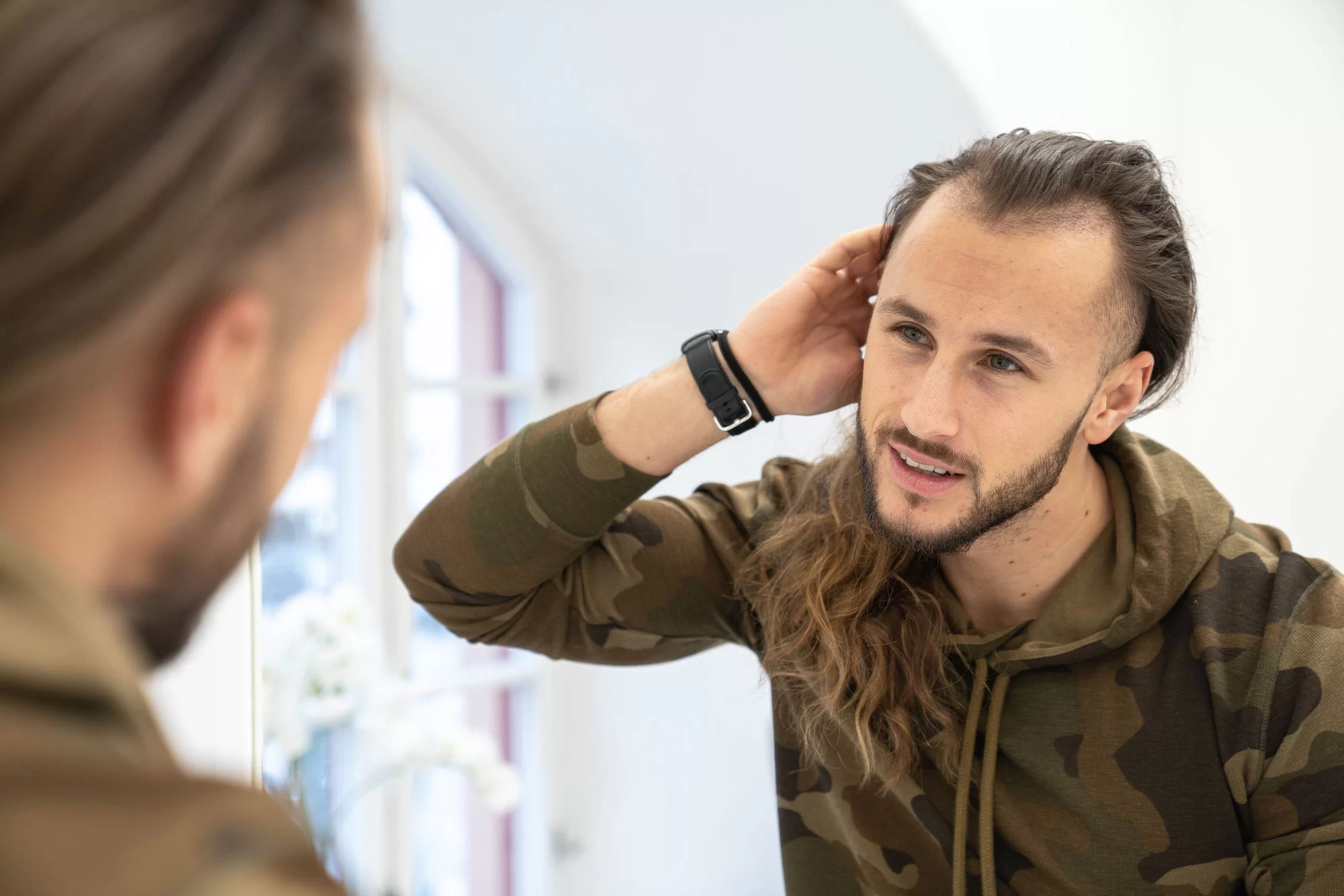 En man med höga vikar tittar sig i spegeln
