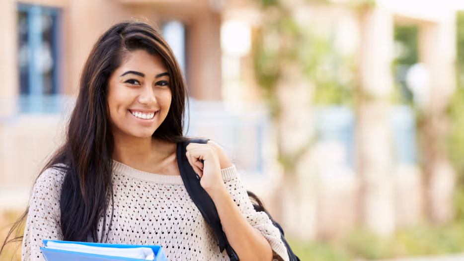 Girl smiling outside, holding books after college accommodations evaluation. 