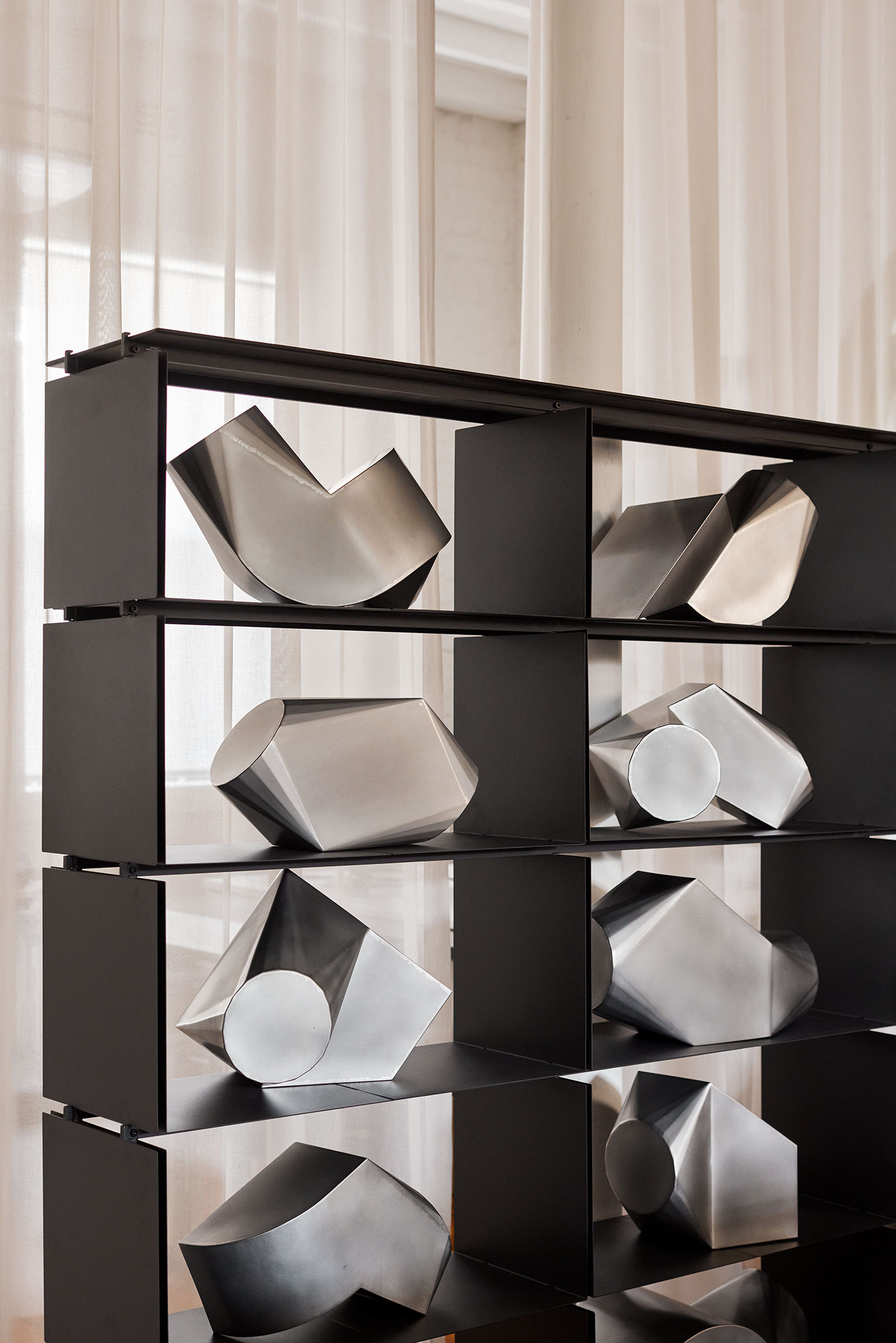 Black shelving unit displaying multiple shiny abstract metallic sculptures with geometric shapes.