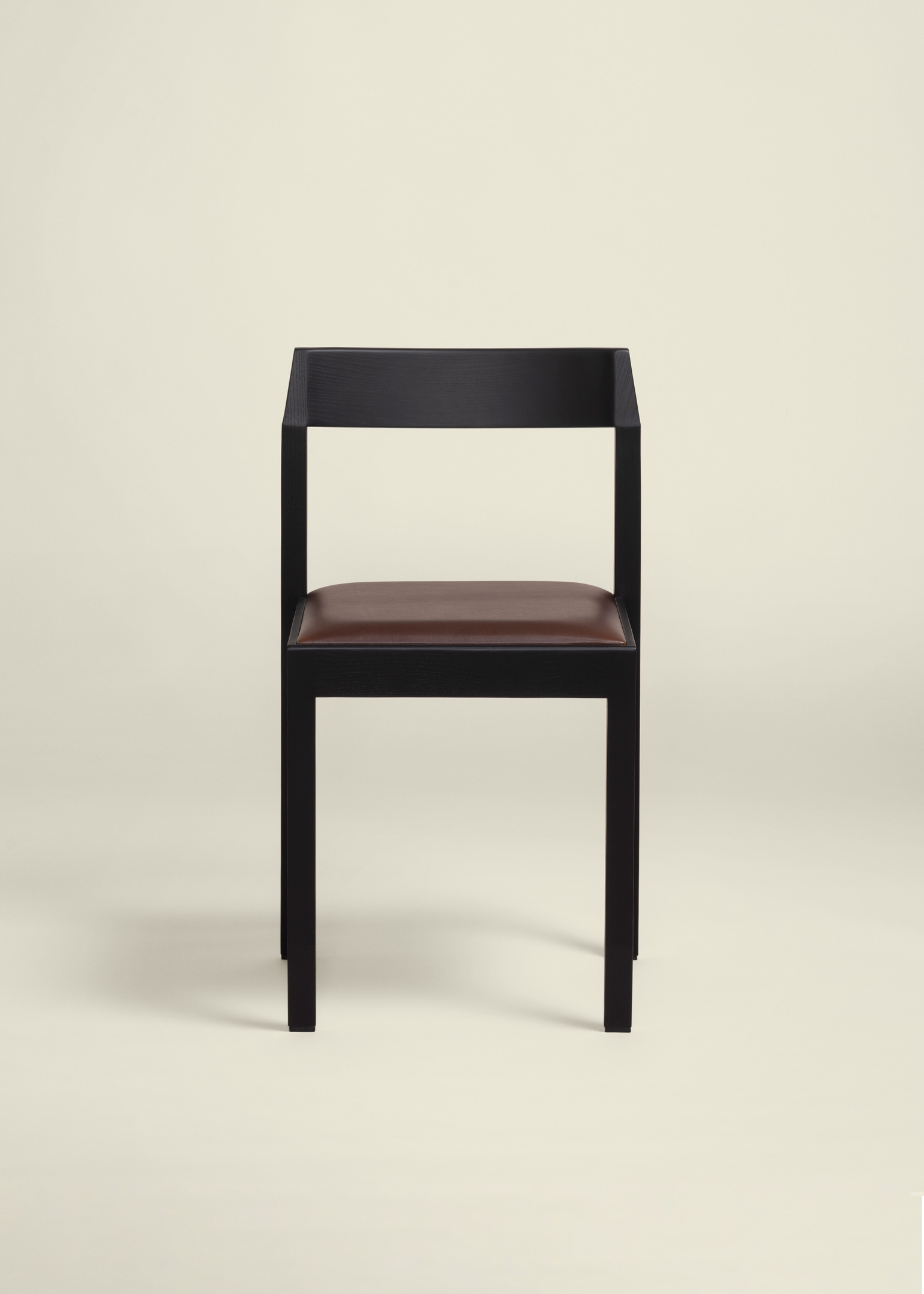 Minimalist chair with a black wooden frame and a brown cushioned seat, viewed from the front against a light beige background.