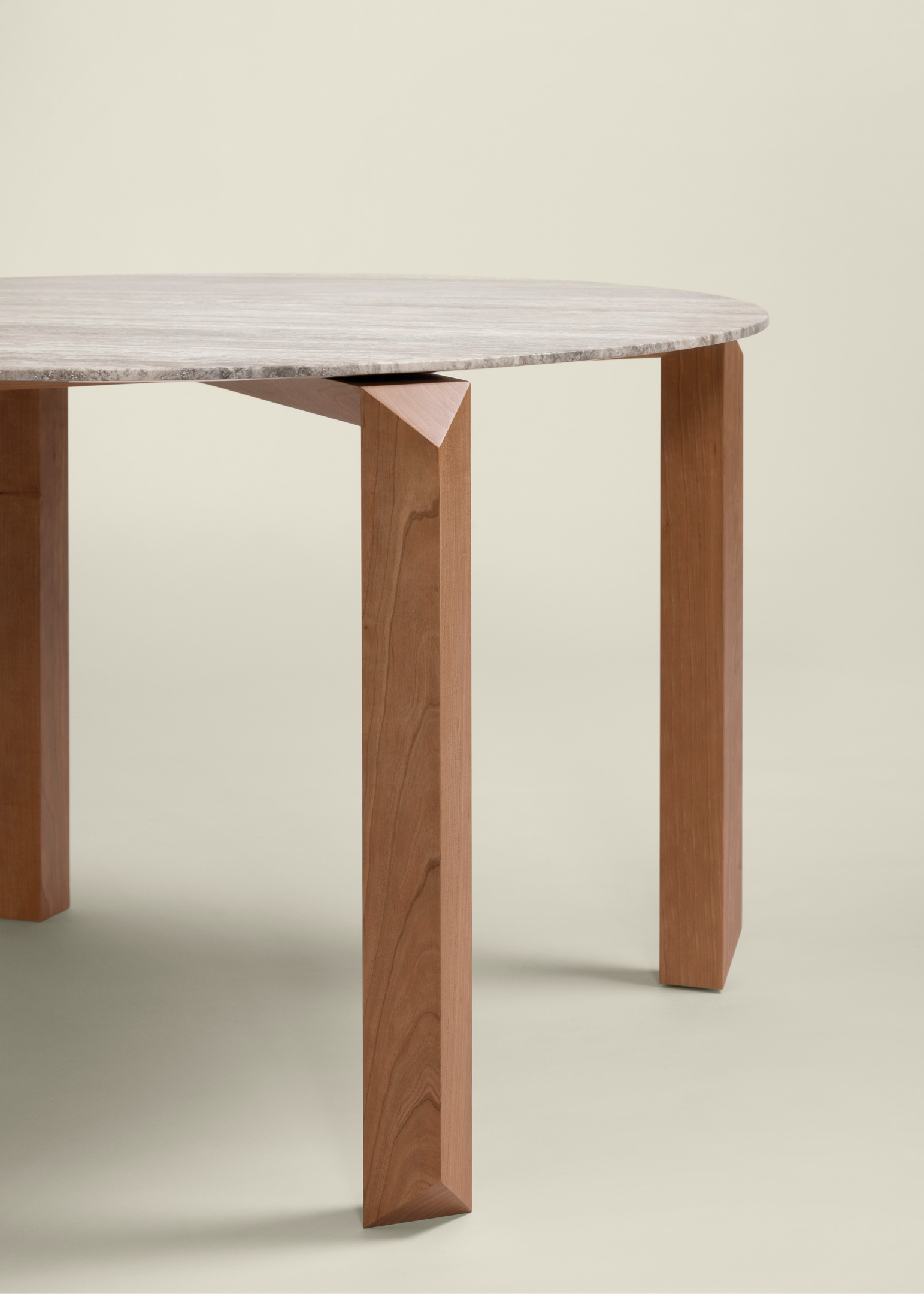 Close-up of a modern round table with a light-colored marble top and angled wooden legs with a warm reddish tone.