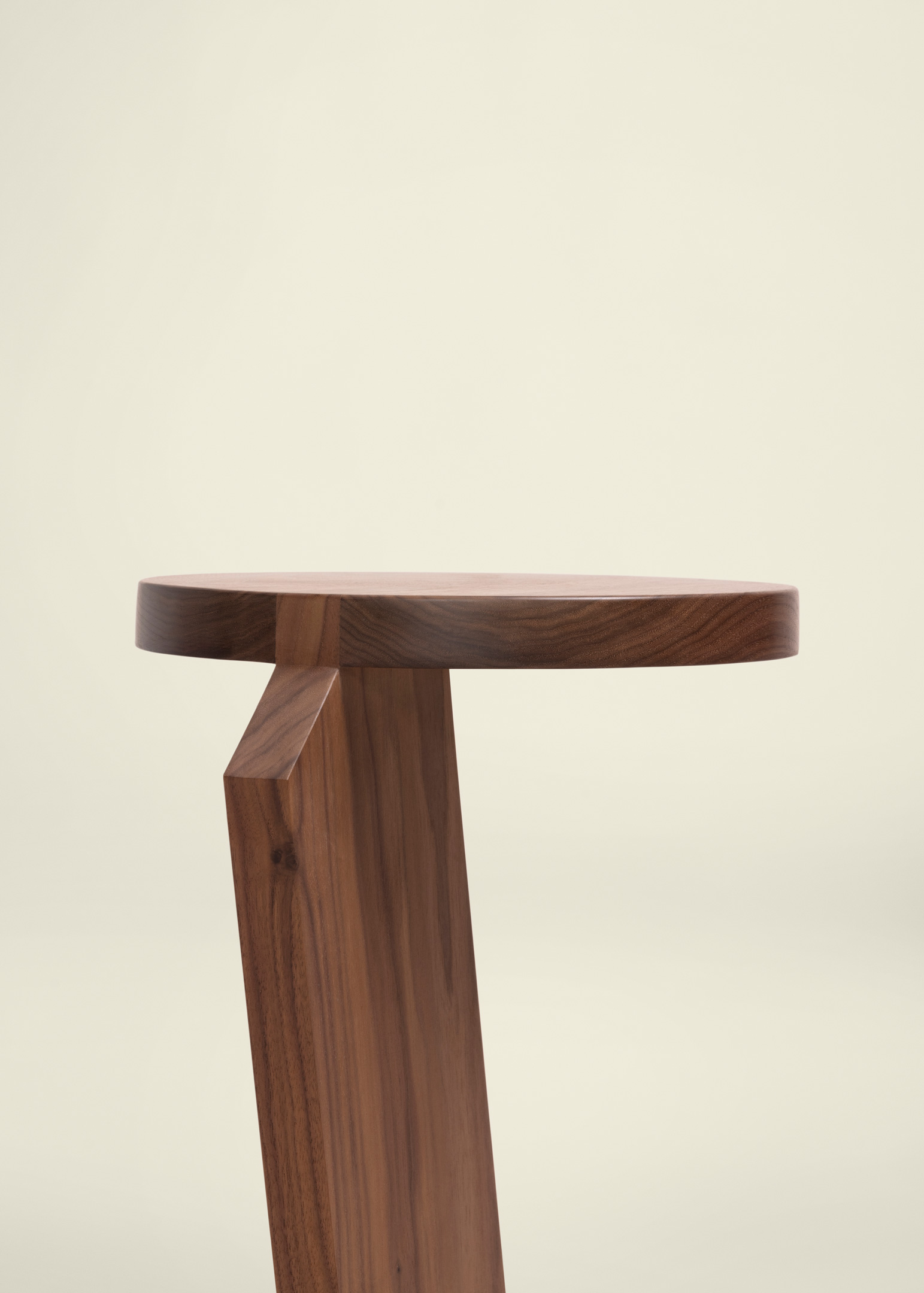 Minimalist wooden side table with a round top and a single angled leg in a warm brown finish against a plain light background.