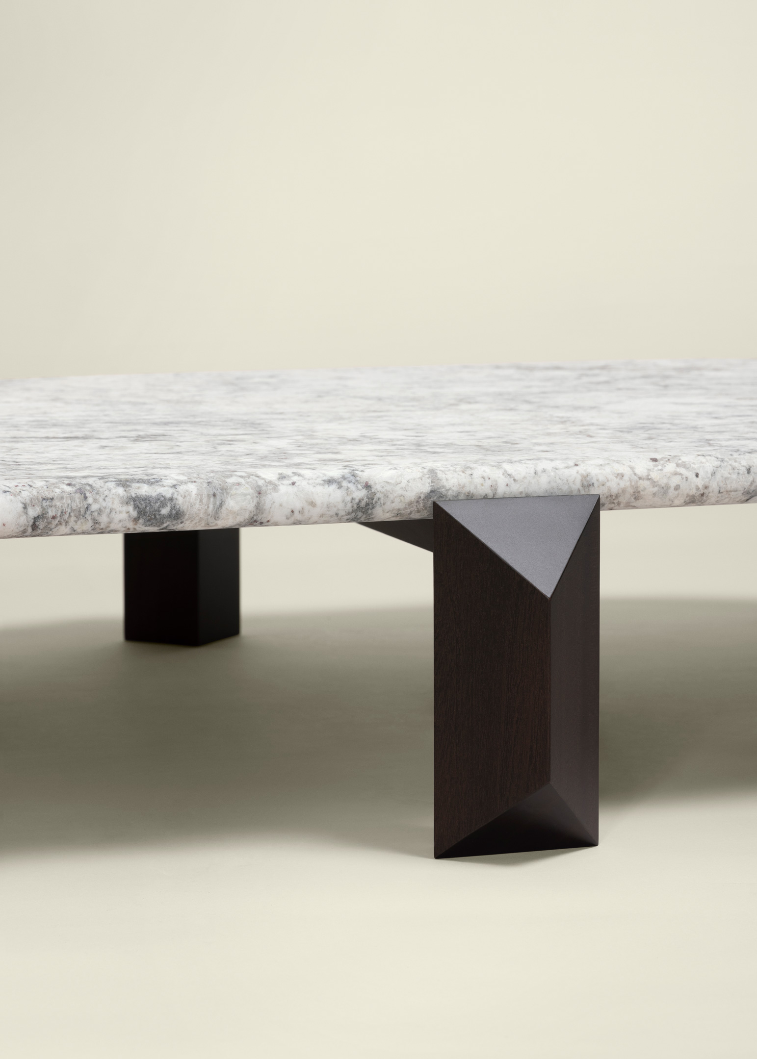 Close-up of a table with a thick white and gray marble top and a dark, faceted geometric wooden leg.
