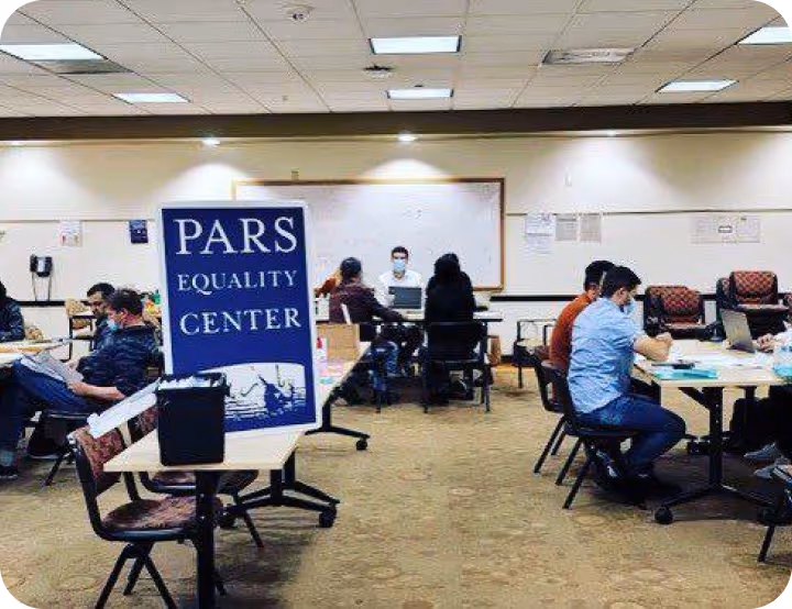 Indoor room with people sitting at tables working or studying, with a sign reading 'PARS Equality Center' prominently displayed on a stand.
