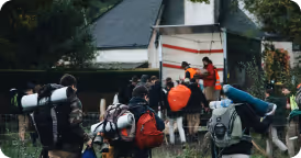 Group of hikers with backpacks gathered near a truck unloading gear in front of a cabin.