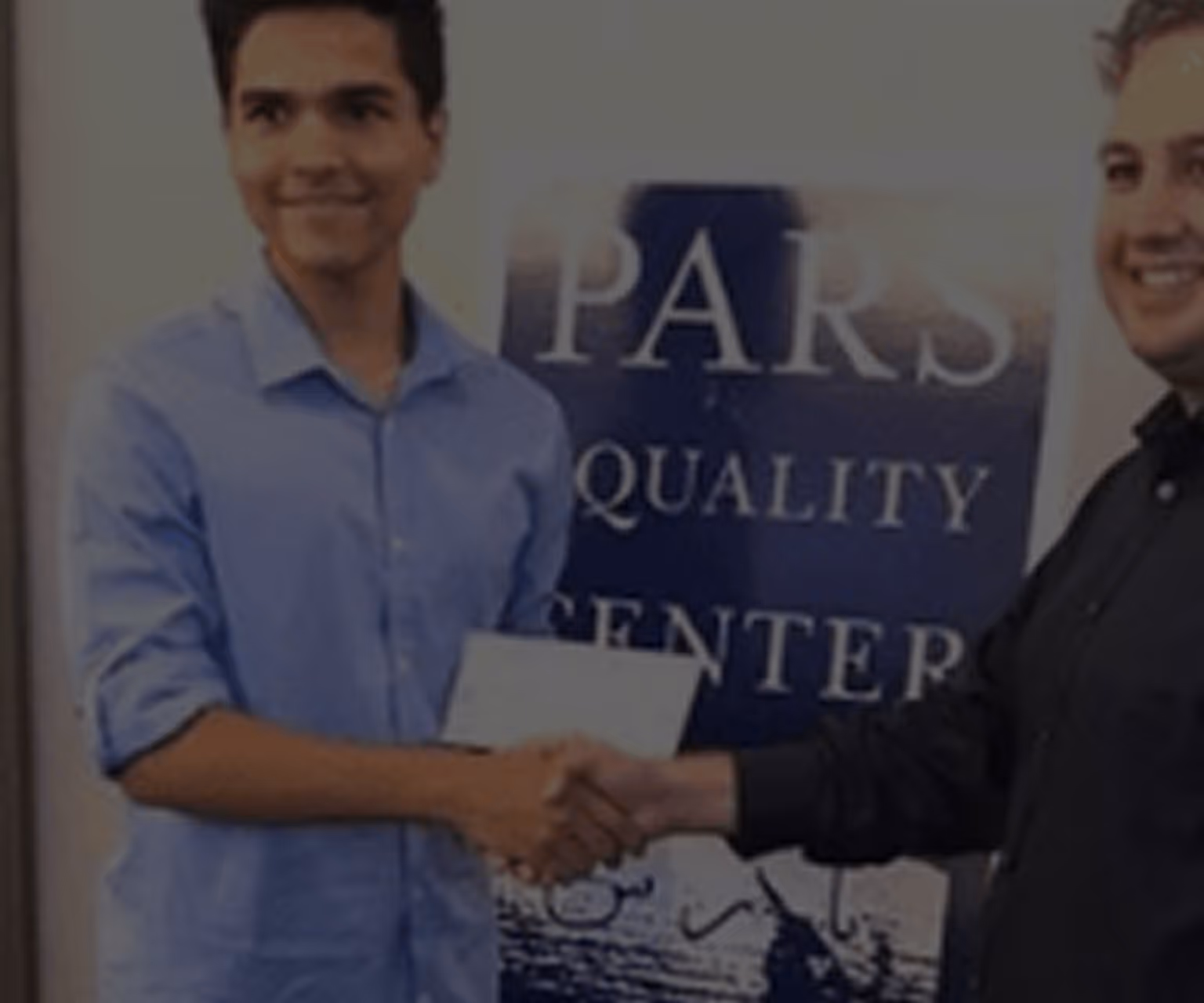 Two men shaking hands in front of a sign that reads 'PARS QUALITY CENTER'.