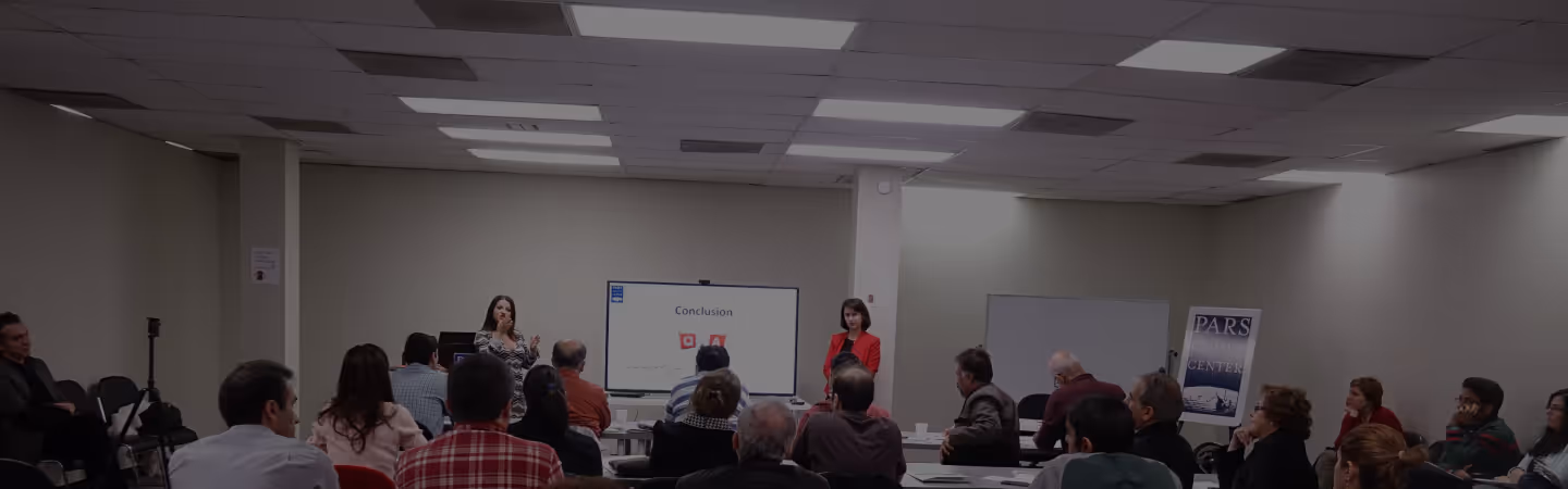 Two presenters speaking to an audience in a conference room with a digital screen displaying the word 'Conclusion'.