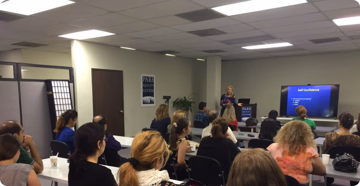 A woman giving a presentation on self confidence to an audience seated in a conference room at Pars Equality Center.