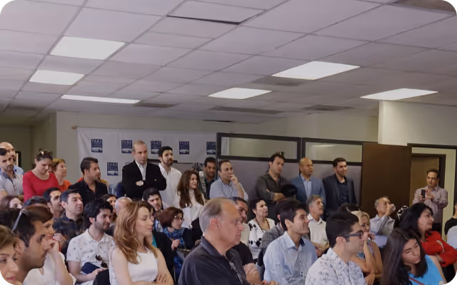 A diverse group of people attentively listening in a brightly lit conference room.