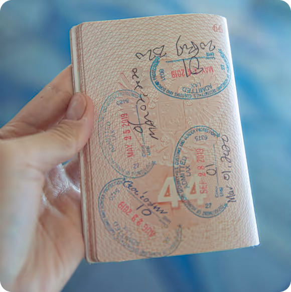 Hand holding a passport page stamped multiple times with travel dates and handwritten notes.