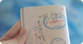 Hand holding an open passport page with multiple stamped visa marks.