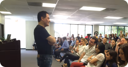 Man standing and speaking to a seated audience in a bright, modern conference room.